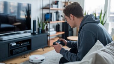 Un homme utilise une manette PS5 pour contrôler un robot aspirateur.